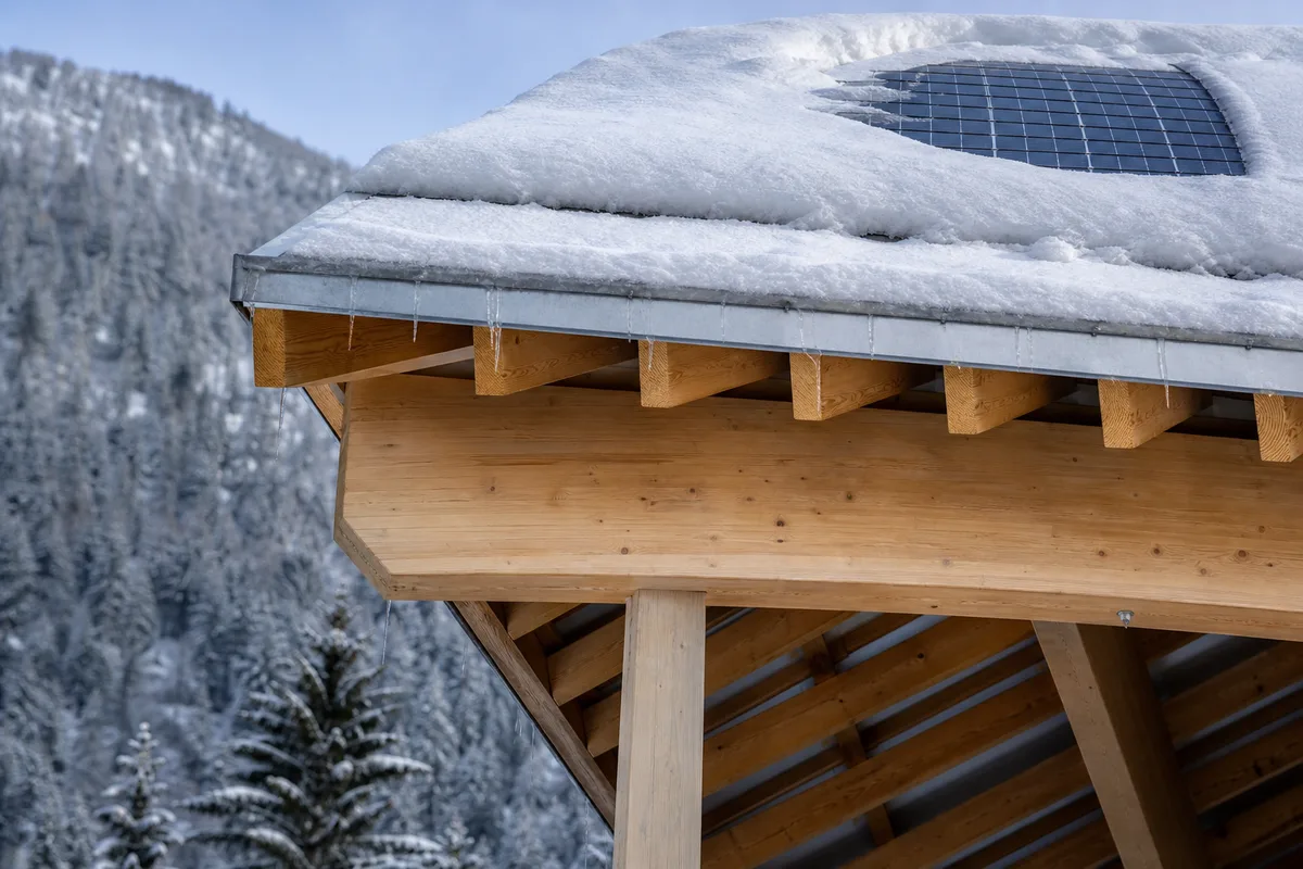 Poutre maîtresse en lamellé-collé et pannes d’un carport bois sous une couche de neige fraîche, montagne en arrière-plan