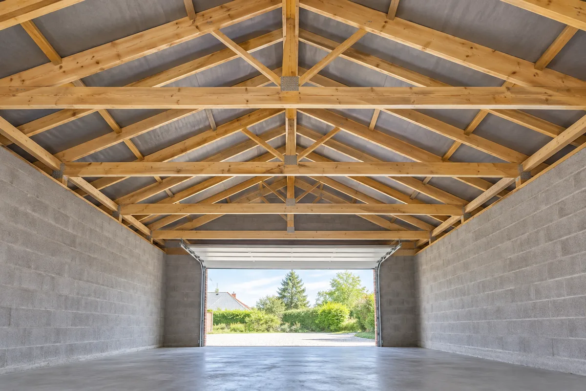 Charpente de garage à deux pans vue de l’intérieur, fermettes reliées par des diagonales