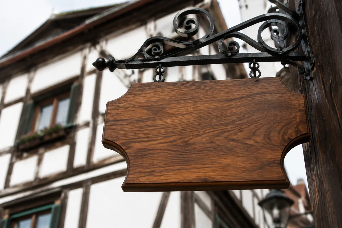 Enseigne en bois gravée suspendue à une potence en fer forgé devant une boutique