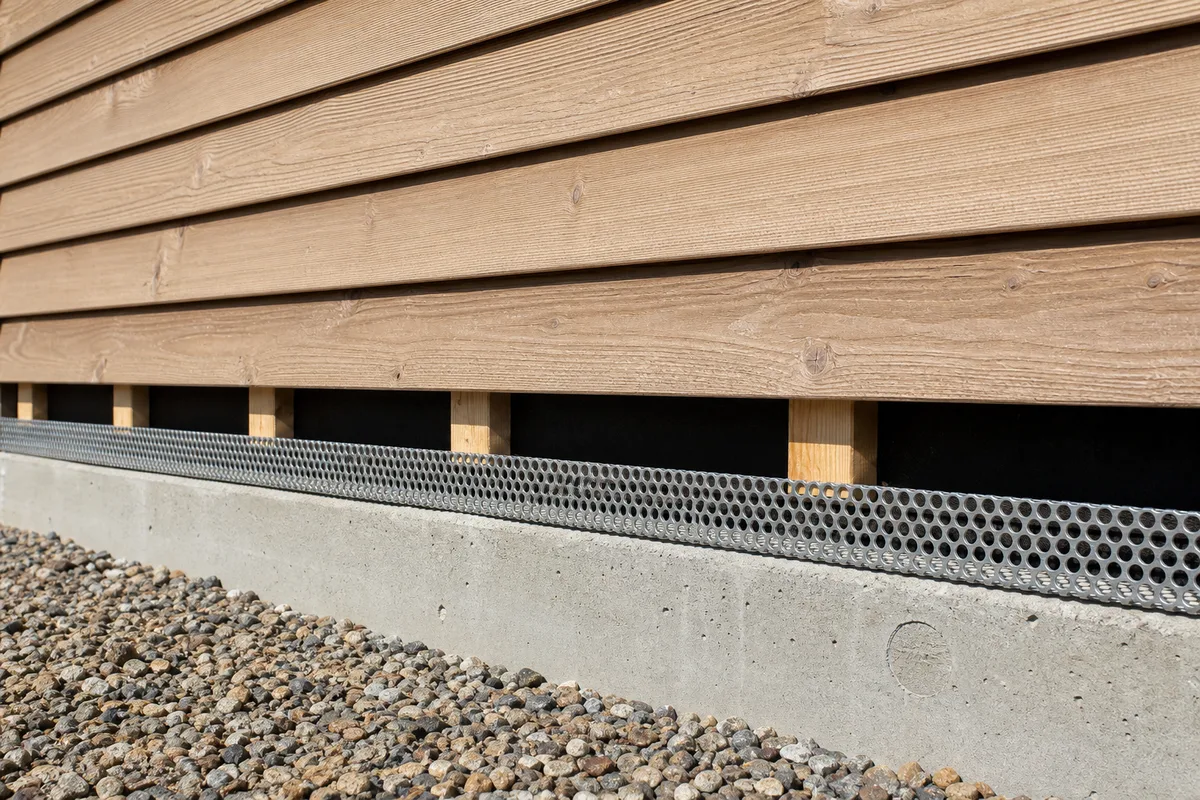Détail de pied de mur bois avec lame d’air ventilée, tasseaux et grille anti-rongeurs