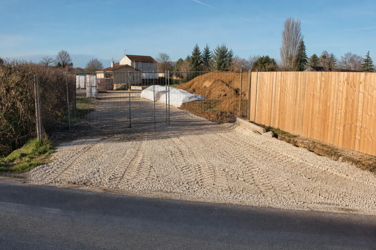 Entrée de chantier stabilisée en grave compactée avec palissade bois et portail en retrait de la route